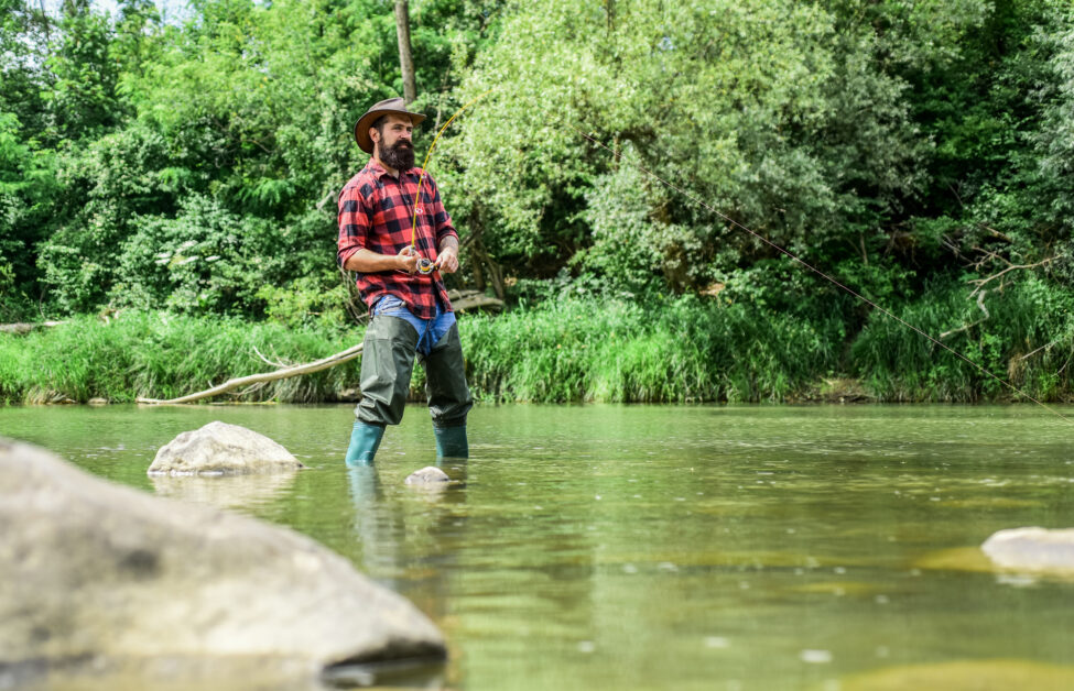 Hobby sport activity. Fish farming pisciculture raising fish commercially. River lake lagoon pond. Trout farm. Fisherman alone stand in river water. Man bearded fisherman. Fisherman fishing equipment.